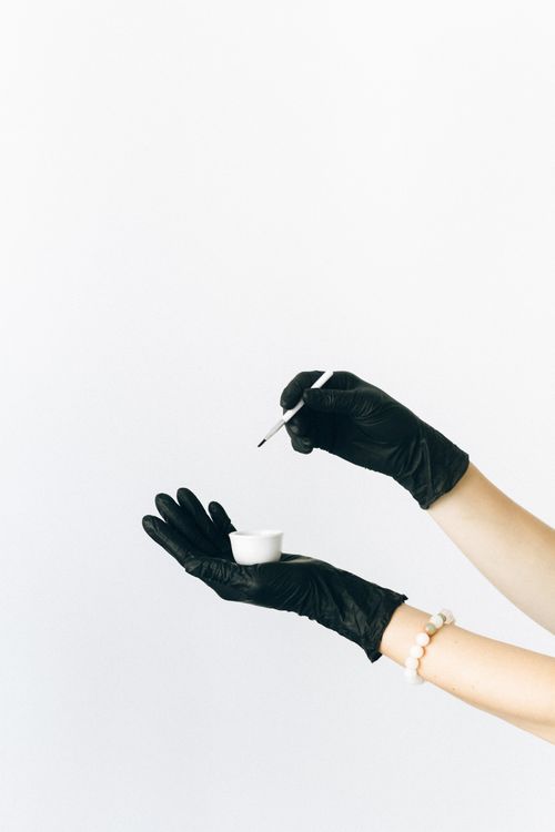 Free Black gloved hands holding a small white cup and brush against a white background. Stock Photo