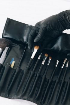 Close-up of a professional makeup brush set with hand in a black latex glove.