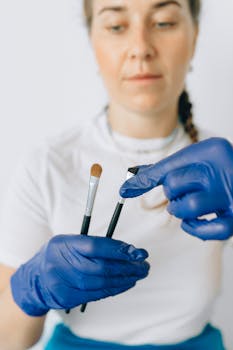 A makeup artist in gloves demonstrating various brushes for precise application.