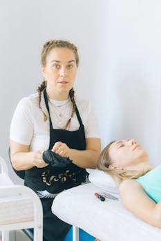 Makeup artist in black apron preparing client for beauty service with makeup tools.