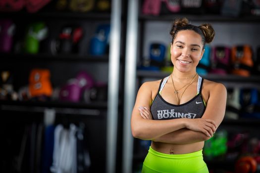 A smiling woman in a sports bra and activewear stands confidently in a gym setting.