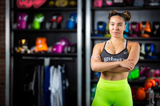 Determined woman in activewear poses among colorful boxing gear in a gym setting.