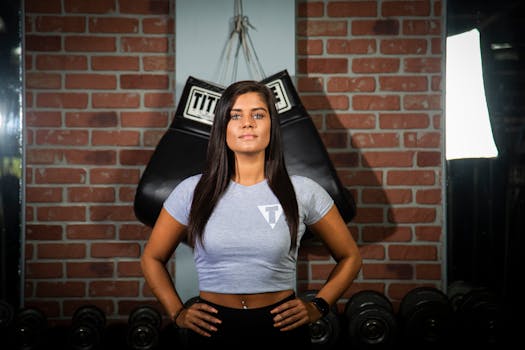 Fit woman in crop top posing confidently in gym with brick wall and equipment.