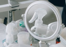 Close-up of cosmetic tools and products on a vanity, including a mirror and spray bottle.