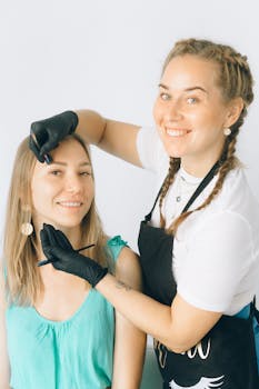 A professional beauty session with a smiling woman applying eyelash extensions to a client indoors.