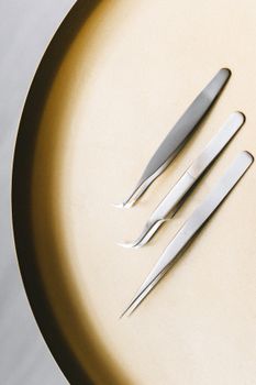 高角度视角下的扁平圆形表面上，摆放着三把不锈钢镊子