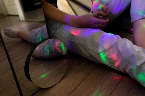 Free Crop unrecognizable person touching hands and sitting on floor surrounded by various mirrors in room with colorful lights Stock Photo