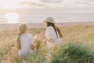 日落时分，两名女子在宁静海滩附近郁郁葱葱的草丛中轻松交谈