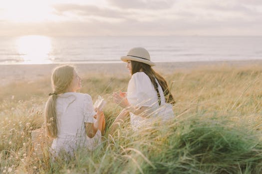 日落时分，两名女子在宁静海滩边的郁郁葱葱草丛中轻松交谈