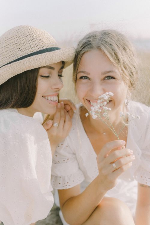 Free Two women sharing a joyful moment outdoors with smiles and white flowers. Stock Photo