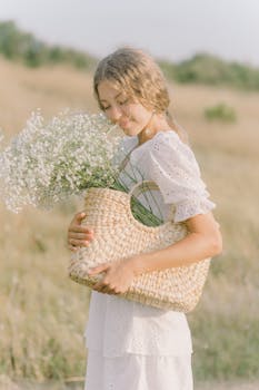 一位年轻的金发女子在阳光明媚的田野里提着一篮白花