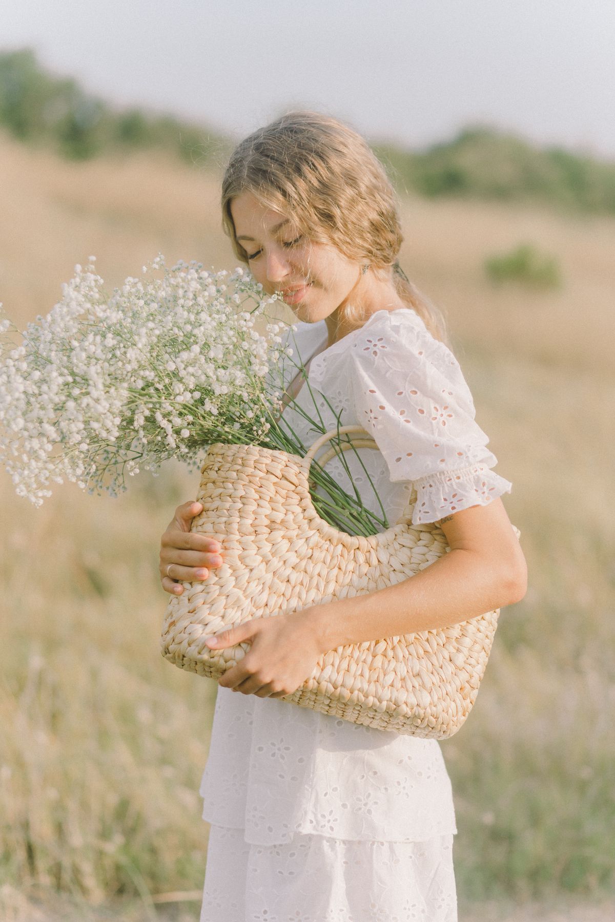 A woman in a white dress carrying a woven basket — styling broderie with natural materials