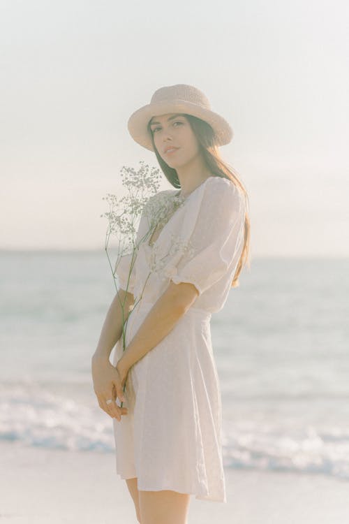 Free A Woman Standing on the Beach while Holding a Flowers Stock Photo