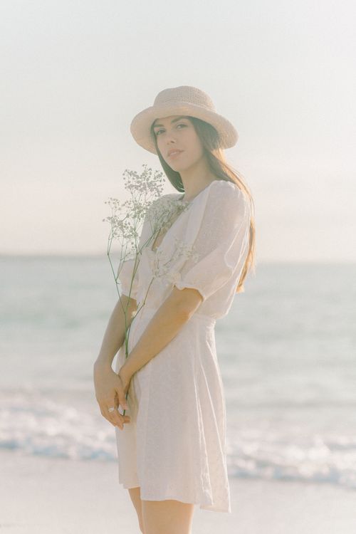 Free Young woman in a boho outfit holding flowers at a sunny beach, exuding a serene summer vibe. Stock Photo
