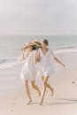 两名身穿白色连衣裙的女子在阳光明媚的海滩上快乐地奔跑，享受着夏日的氛围