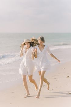 两个女人穿着白色连衣裙，在阳光明媚的海滩上快乐地奔跑，享受着夏日的氛围
