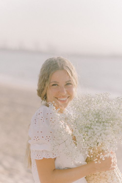 Free Woman in white dress holding bouquet at sunny beach. Stock Photo