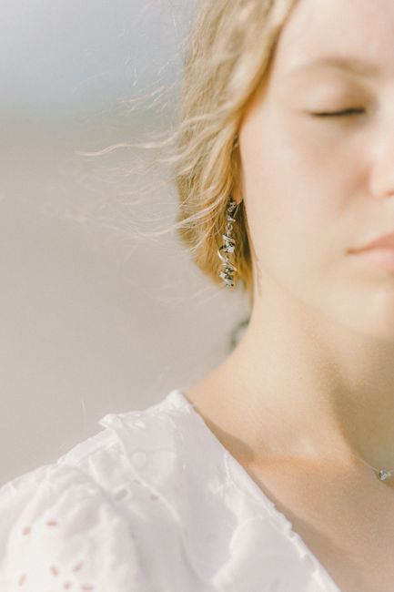A serene close-up portrait of a young woman in soft, natural light with delicate jewelry.