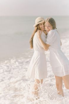 阳光明媚的日子里，两个穿着白色连衣裙的女人在海边笑着拥抱