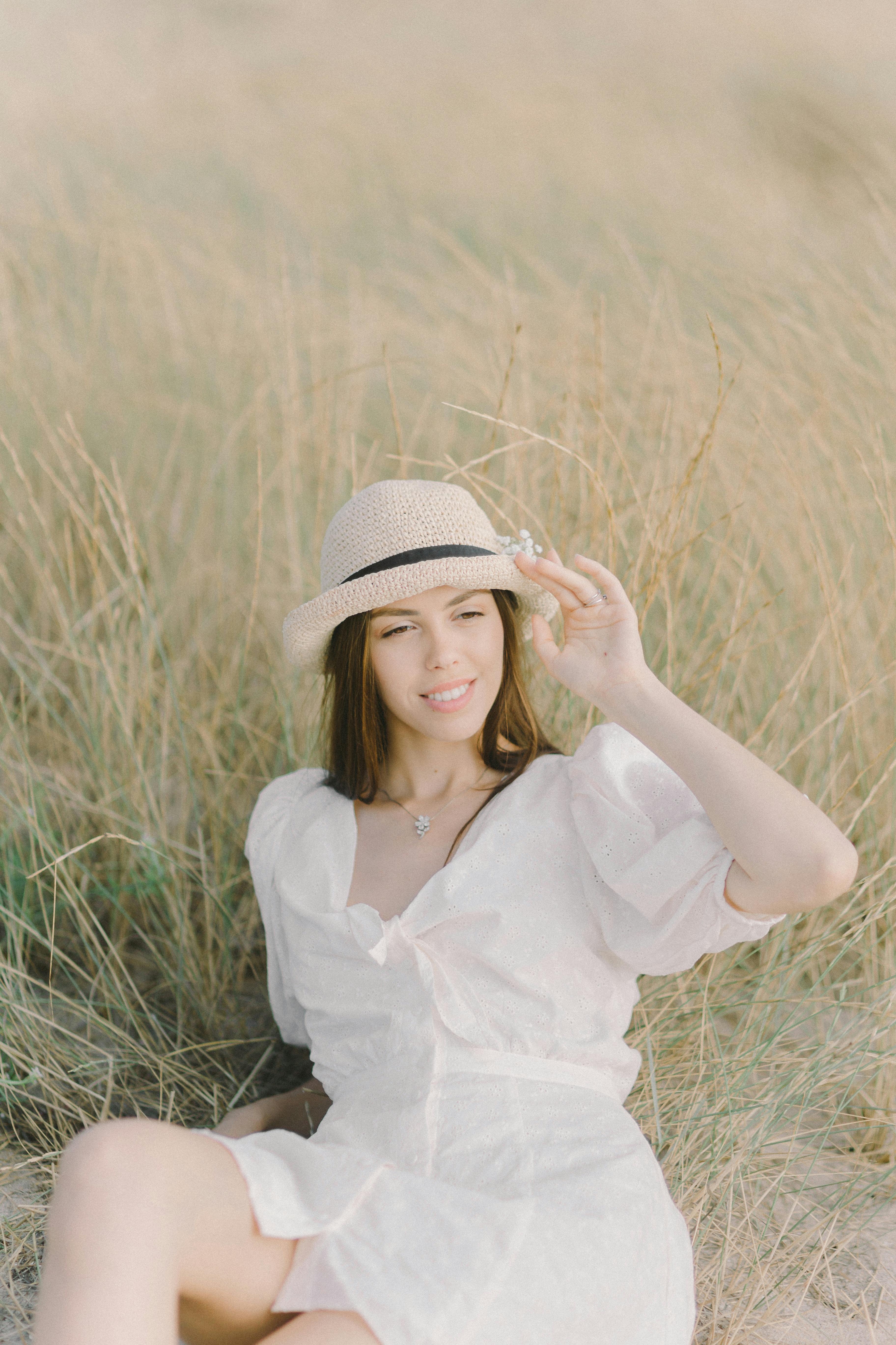 一名身穿白色连衣裙、头戴软毡帽的年轻女子躺在草地上，享受户外明媚的阳光