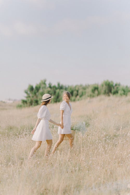Women in White Dress Walking on Brown Field while Holding Each Others Hands