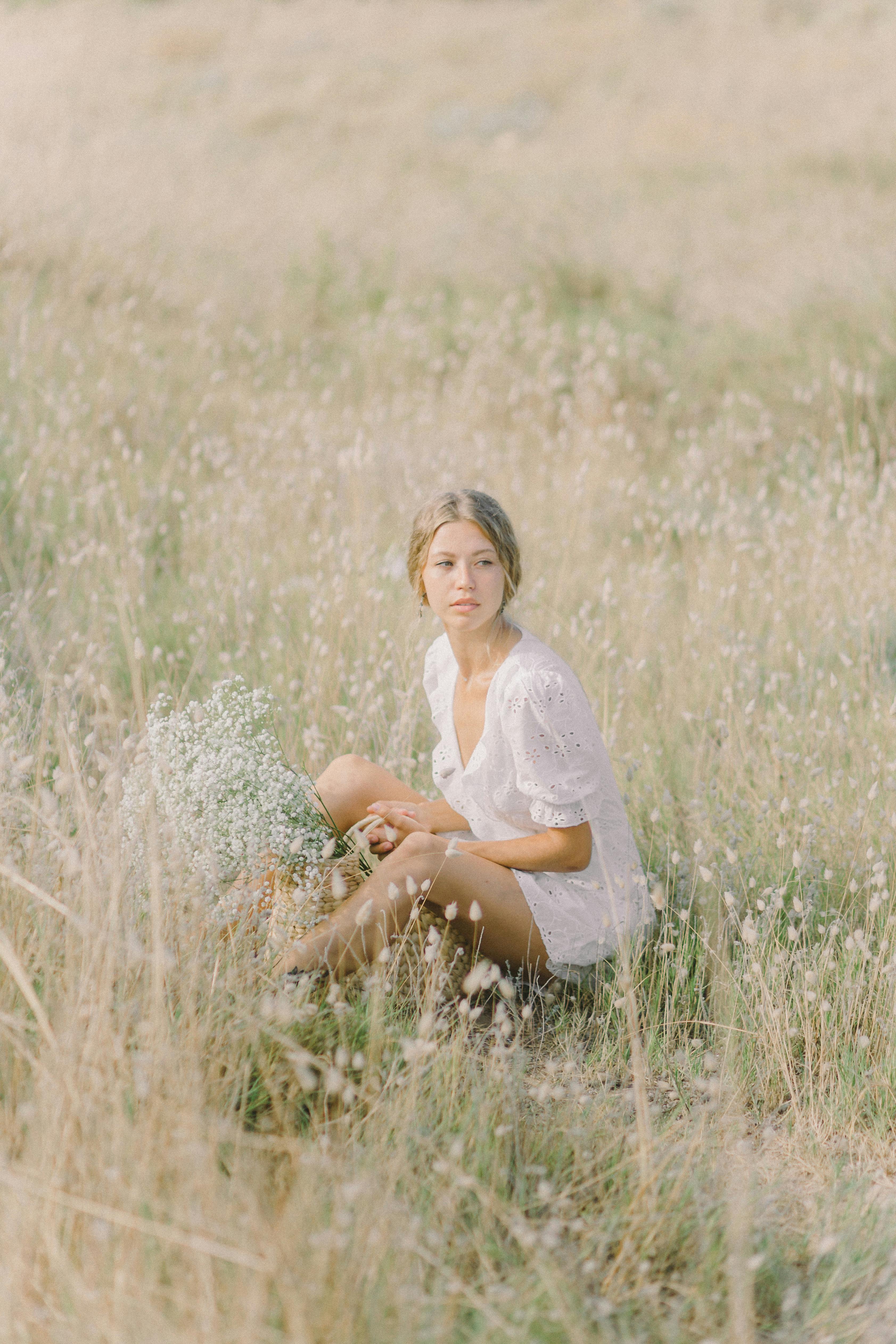 a woman in white dress sitting on grass field while holding a basket