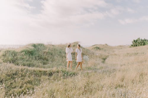 Women in White Dresses Walking on Brown Field while Having a Conversation