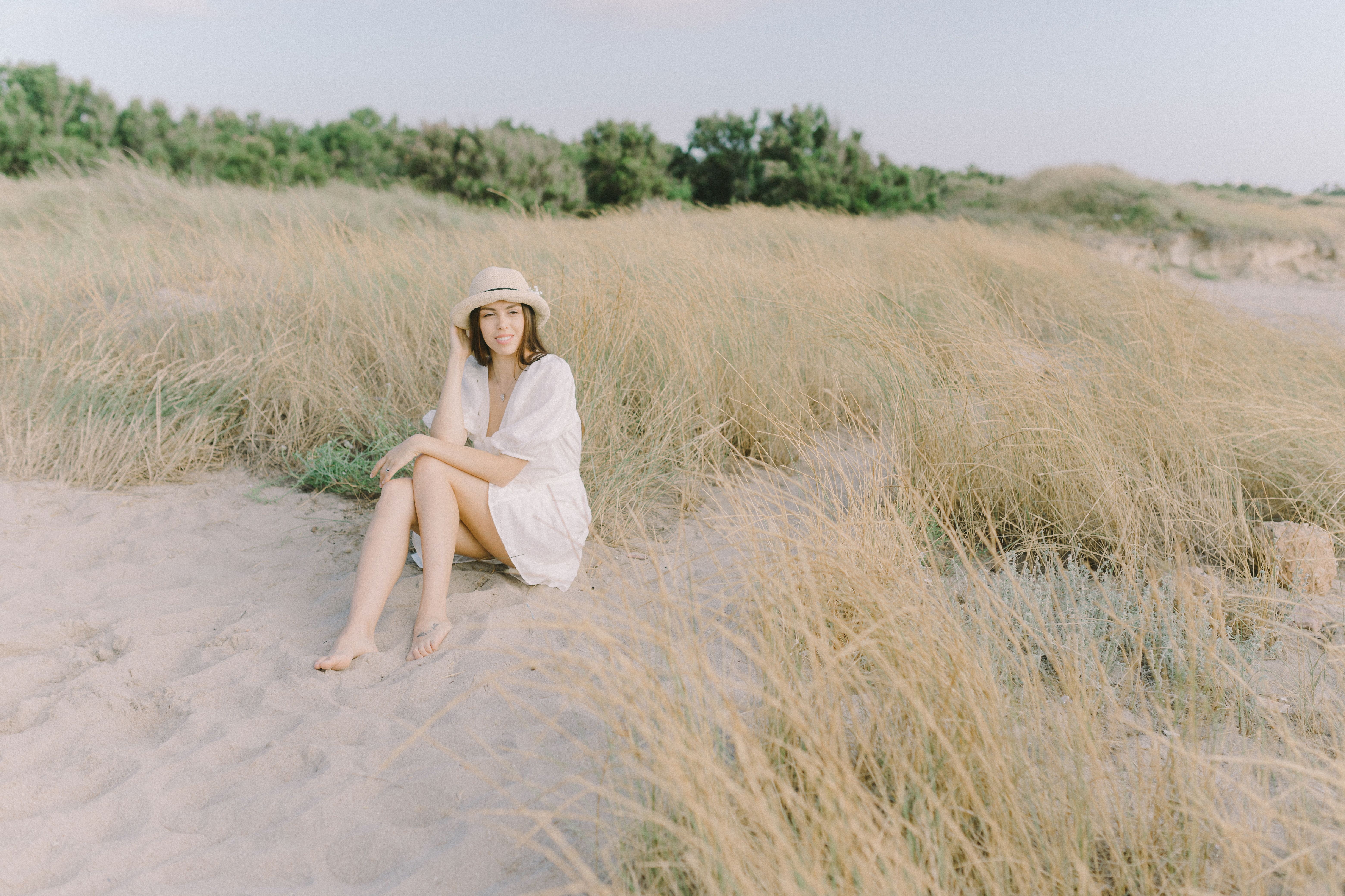A Woman in White Dress Sitting on the Sand Near the Brown Grass · Free ...