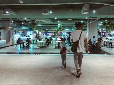 Lively food court scene in urban Thailand with people dining and walking.