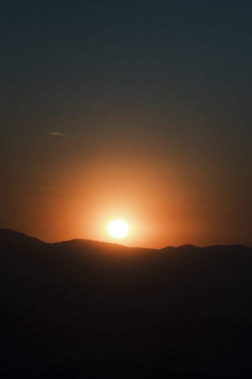 Free A beautiful sunset with a glowing sun setting over tranquil hills under a clear sky. Stock Photo