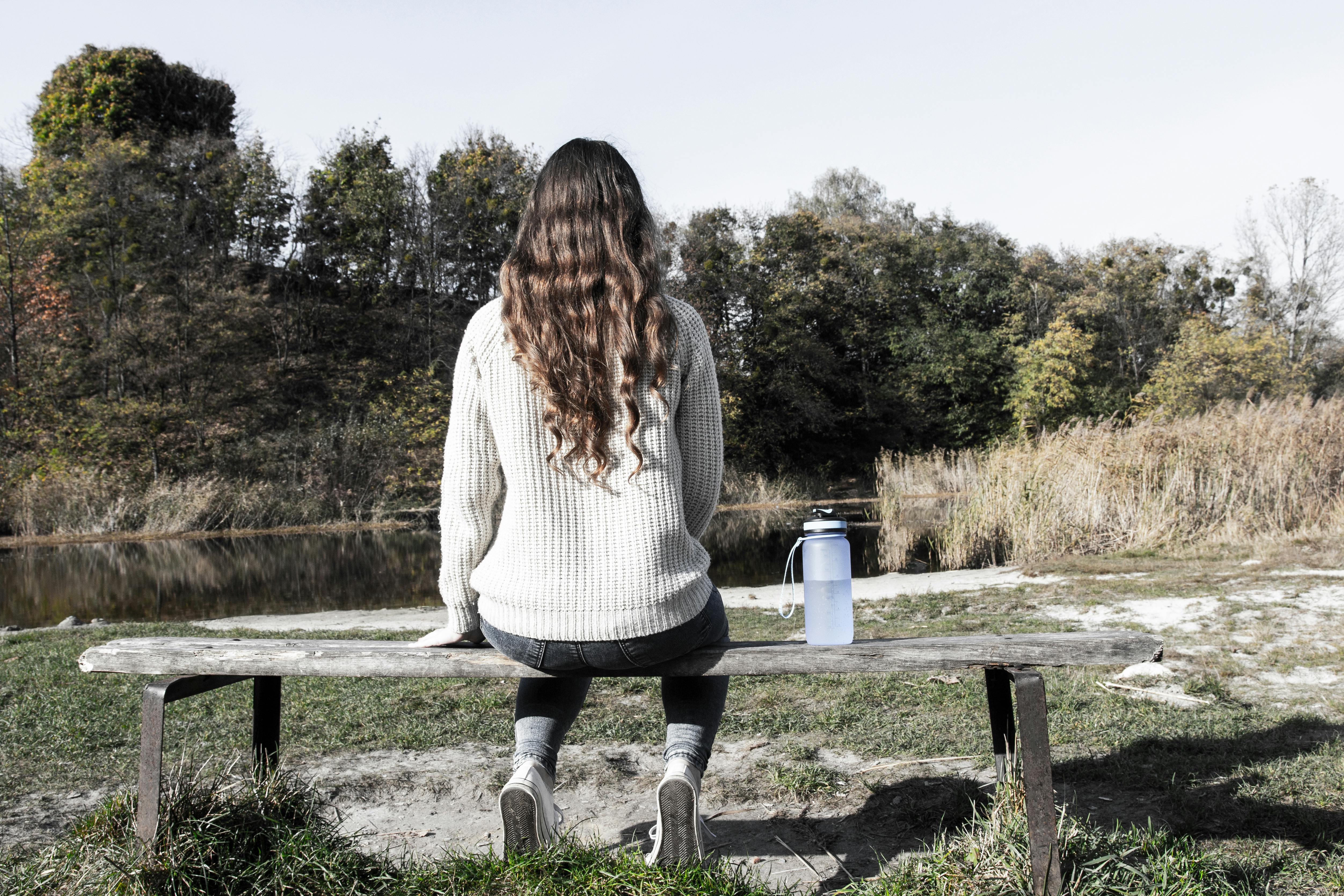 Free Woman in White Sweater and Black Pants Sitting on Brown Wooden Bench Stock Photo