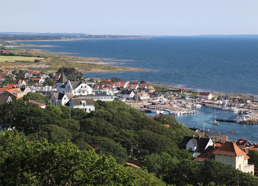 A picturesque view of Mölle's harbor and coastal town in Sweden with lush greenery and clear blue sea.