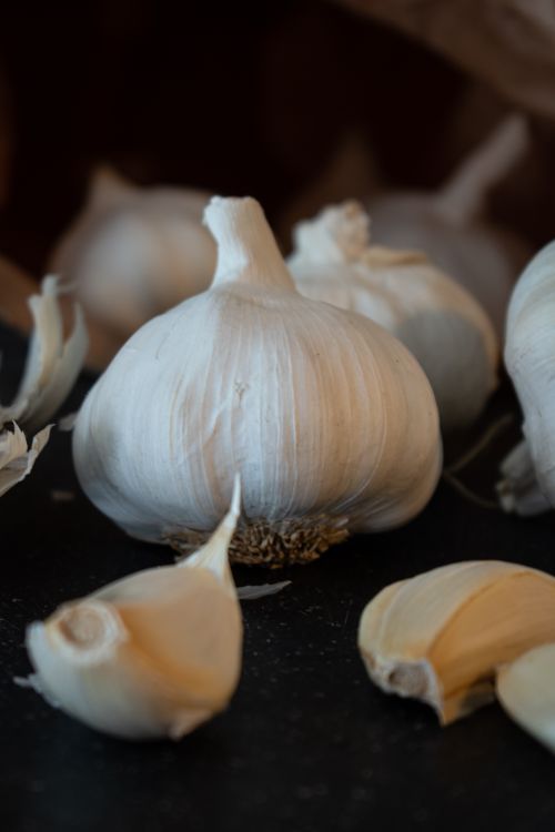 Free Detailed close-up of fresh organic garlic bulbs and cloves on a dark background, perfect for food blogs. Stock Photo