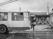 Man in Black Jacket and Pants Walking on Sidewalk Near White and Blue Train