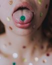 Crop anonymous woman with multicolored smiley paper stickers on face and neck opening mouth and showing sticker on tongue