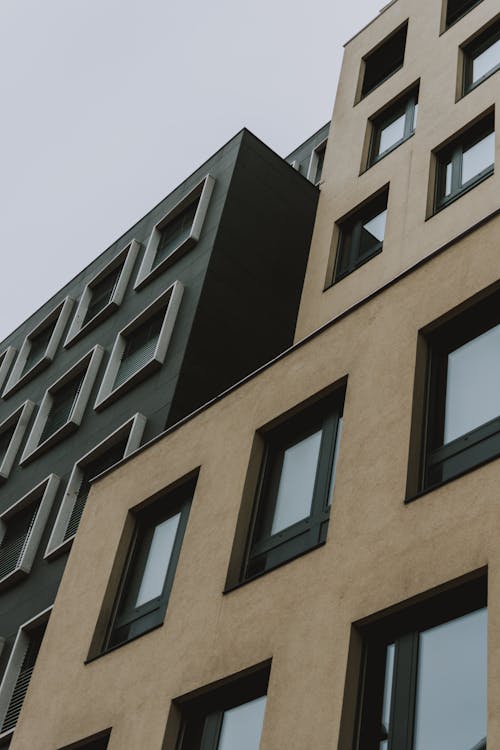 Free From below contemporary building with brown and black facade and windows against gray sky at daytime Stock Photo