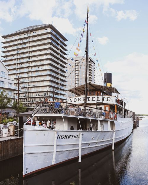 Free A historic steamboat docked in Norrtälje harbor, with modern buildings in the background. Stock Photo