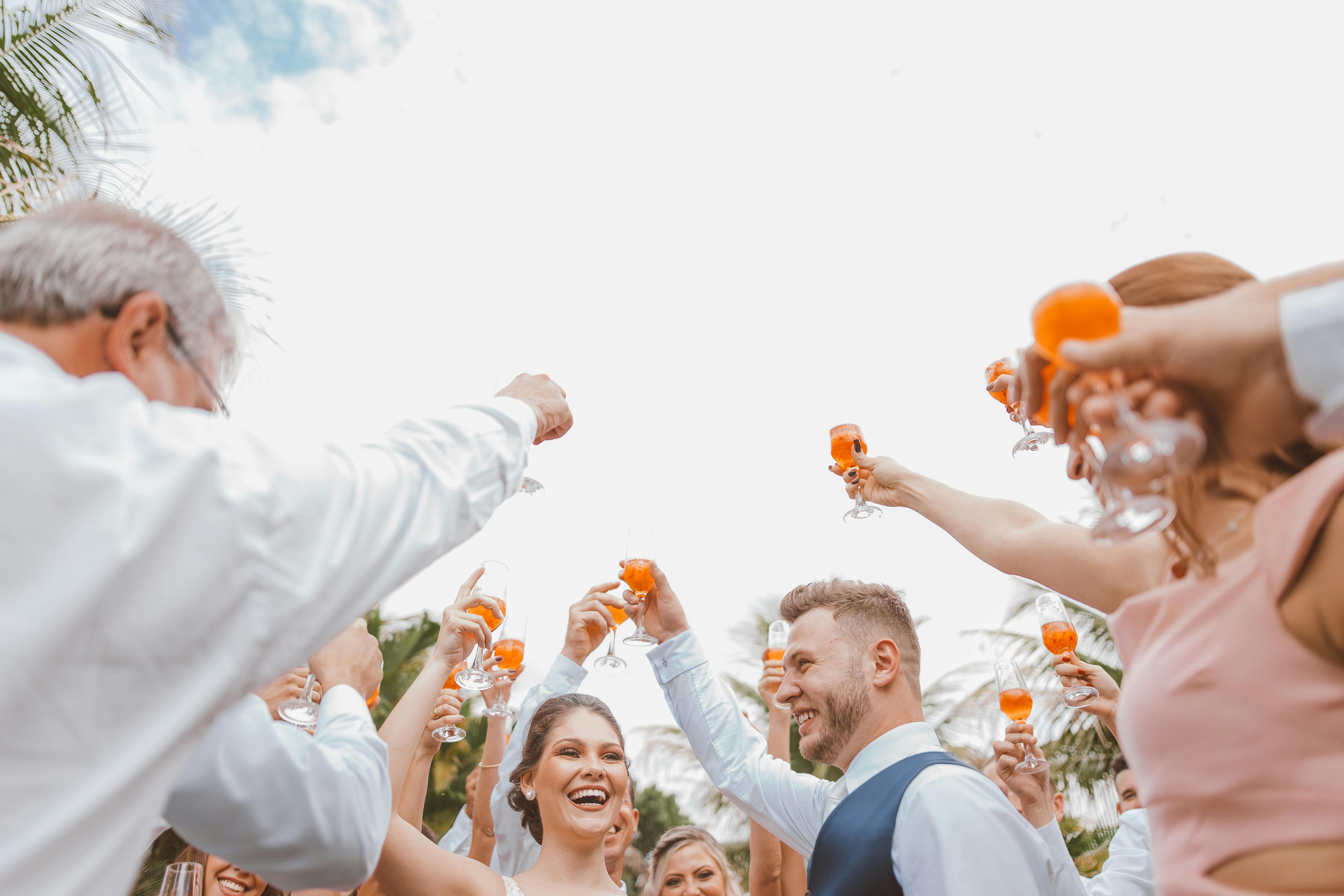 A happy bride and groom toasting with friends at an outdoor wedding celebration.