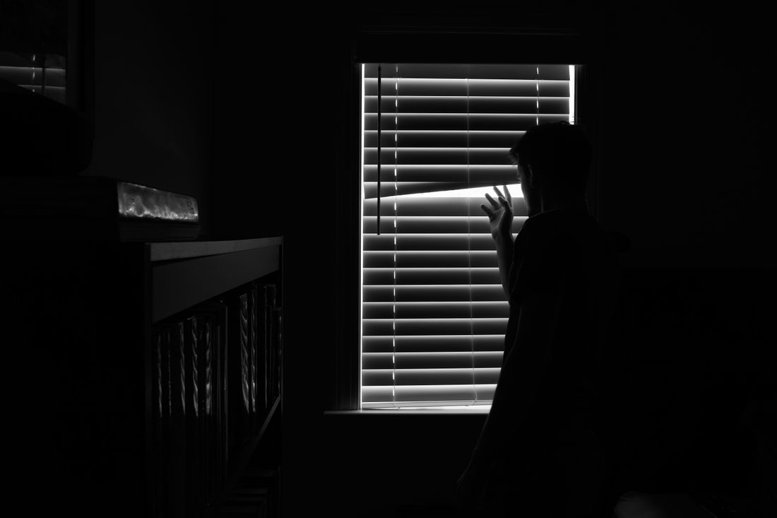 A figure silhouetted against a slatted window in a darkened room — photo by Aidan Carrozza on Pexels