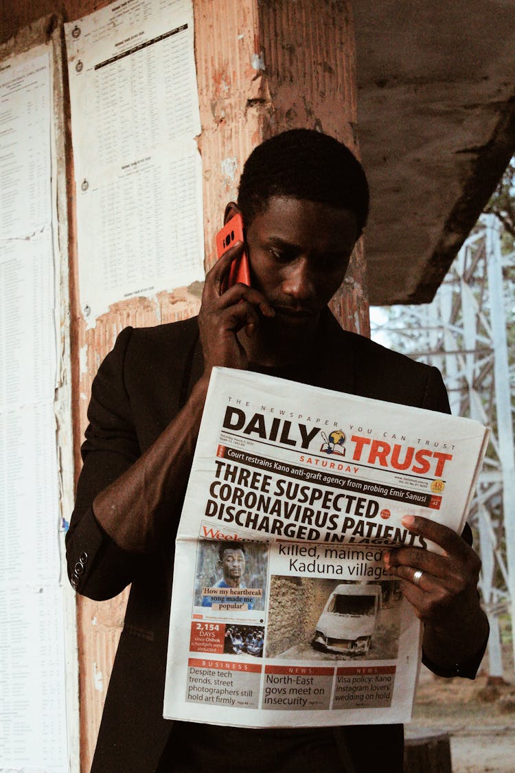 Black Man Speaking On Phone While Reading Newspaper