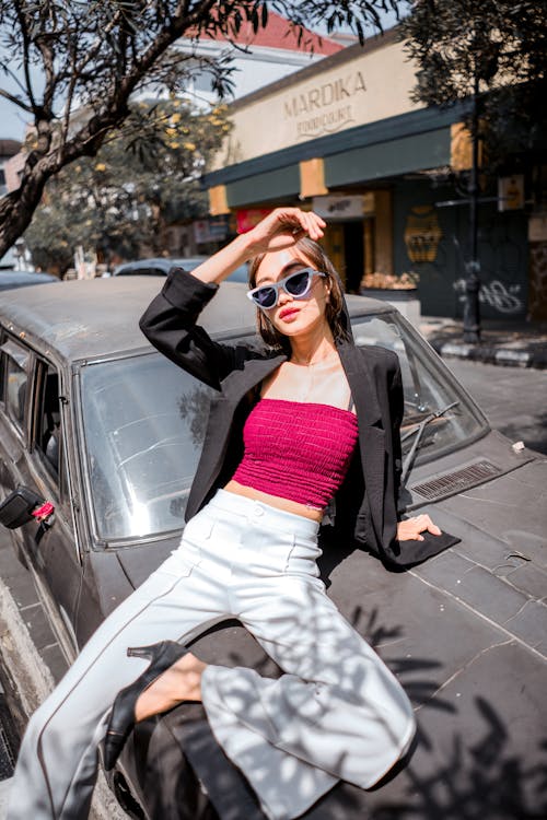 Fashionable young woman sitting on car hood
