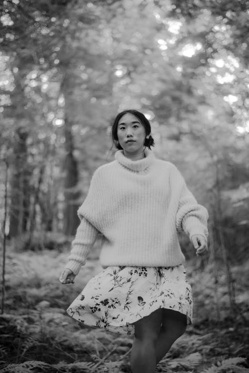 Black and white of Asian woman in oversized wool sweater and skirt walking alone in woodland