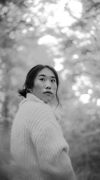 一位穿着羊毛衫的年轻亚洲女子，在宁静的森林中若有所思地凝视着远方