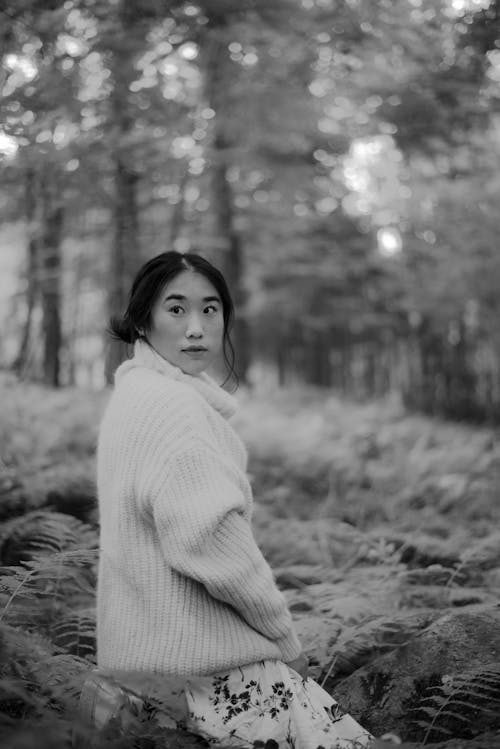 Asian woman in skirt and sweater in forest and fern field