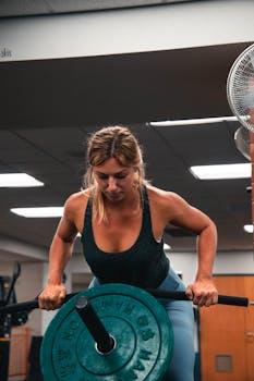 Focused woman lifting a barbell during a workout session in a gym setting.