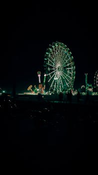 A vibrant nighttime view of an illuminated ferris wheel in an amusement park.