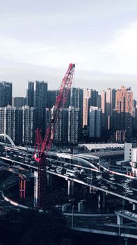 A cityscape with a red crane and bustling traffic below towering skyscrapers, showcasing urban development.