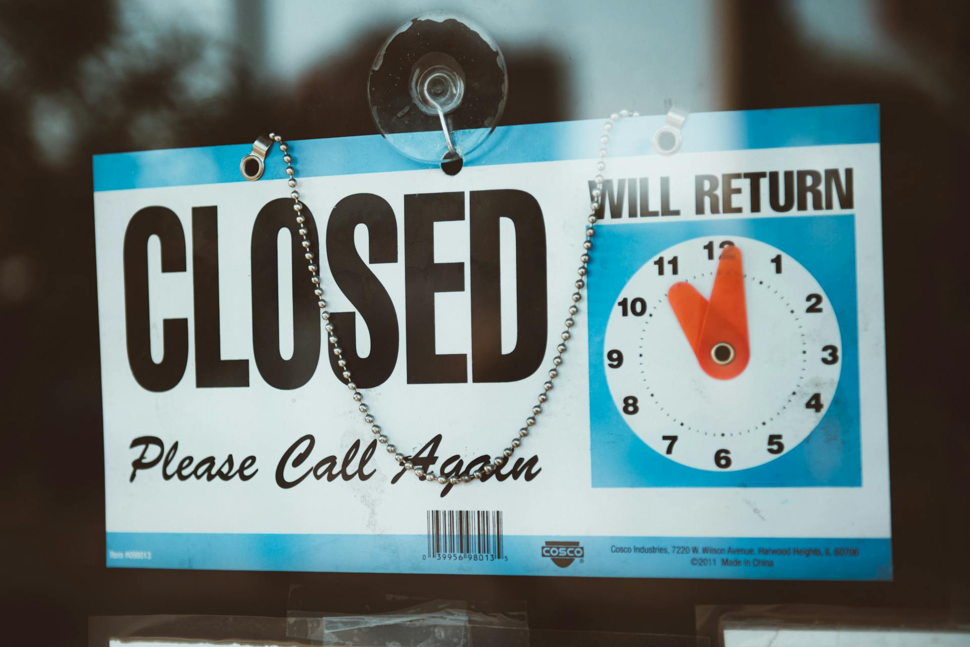 A close-up view of a 'Closed' sign on a door, displaying a return time.