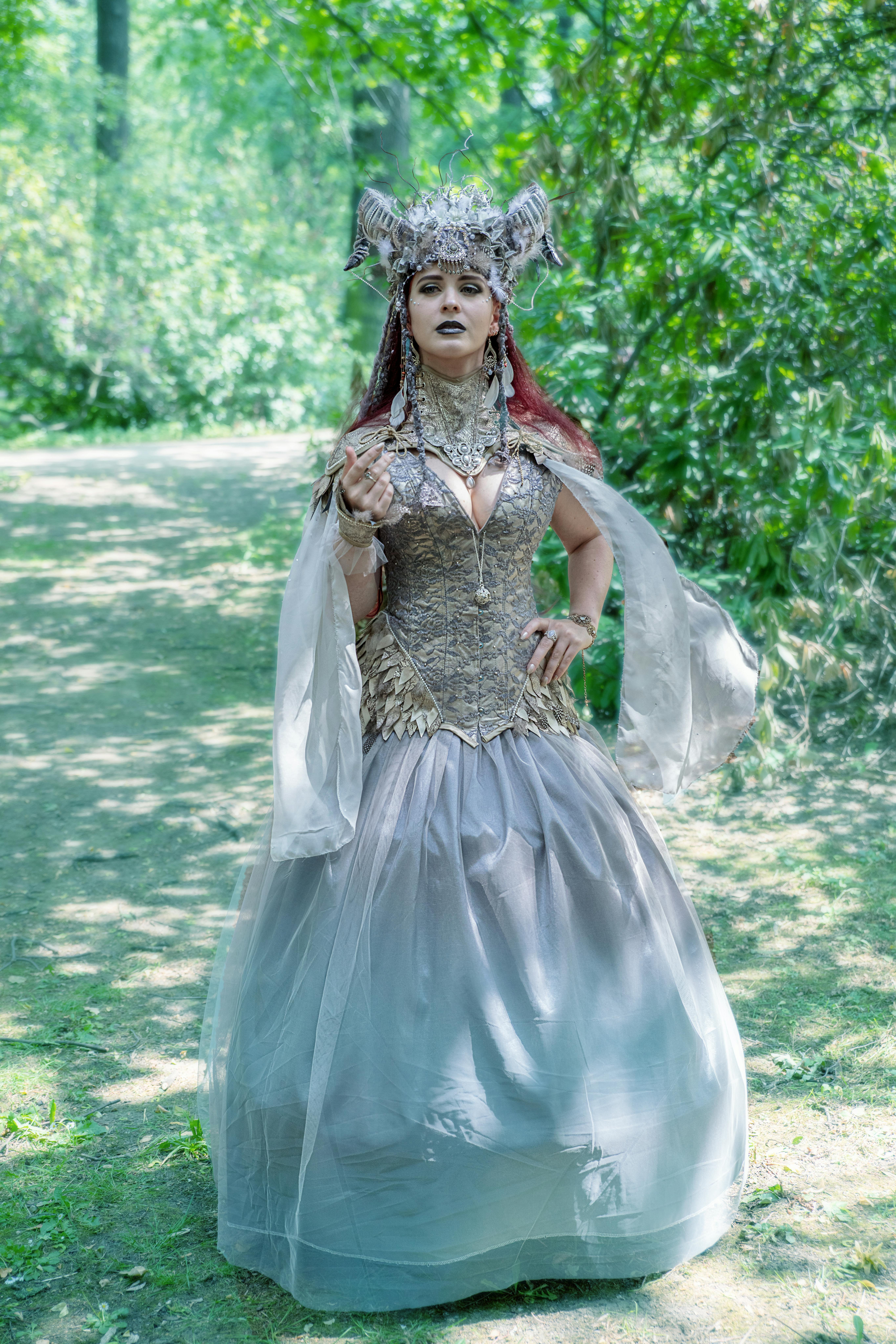 Elegant woman in a fantasy costume posing in a lush forest setting.