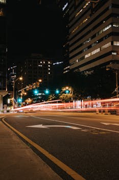Dynamic night view of a city street with vibrant light trails and illuminated buildings.
